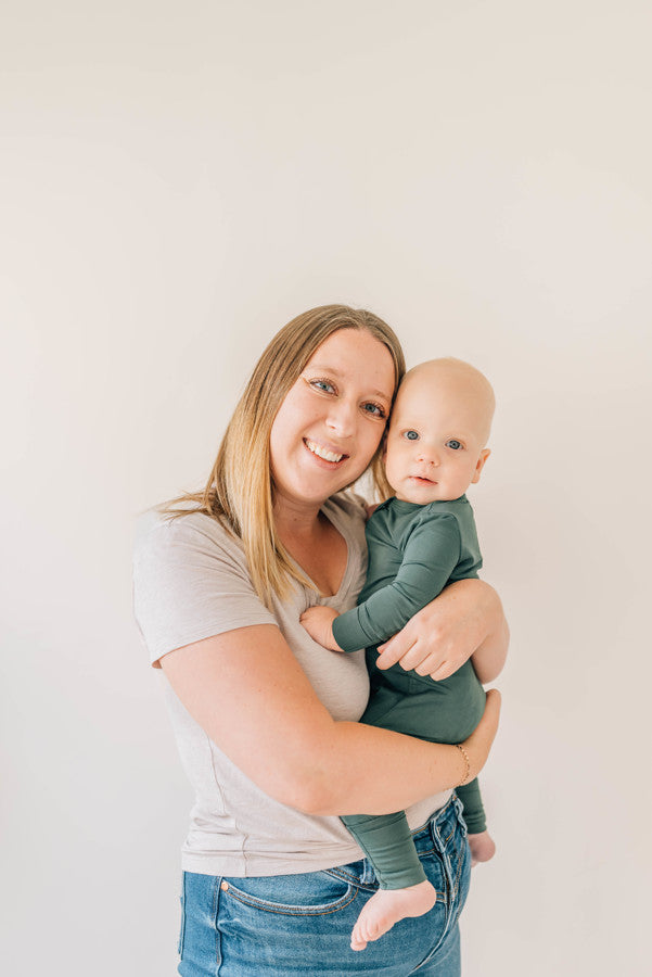 Baby Wearing Luna Luz Two-Way Zip Pajama Romper in Pine Held by Mother